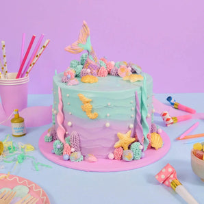 Mermaid Cake with pastel ombre icing, edible mermaid tail, seashells, and piped decorations by Crumbs & Doilies.